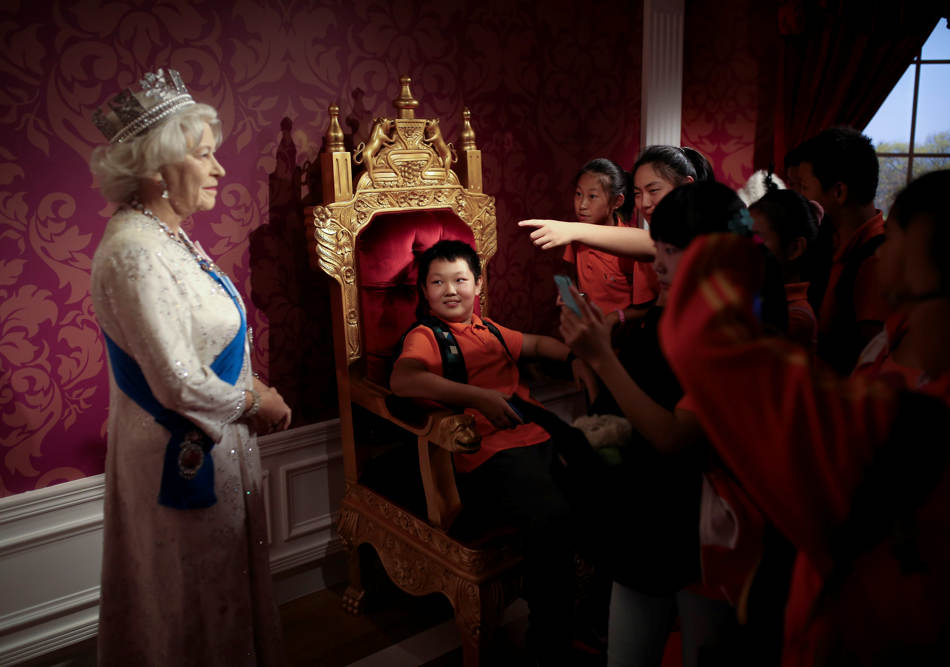 A student, center, sitting on a mock-up of the royalty chair, looks at a wax figure of Britain's Queen Elizabeth II, while others take souvenir photos, at the Madame Tussauds Museum in Beijing, China Friday, Sept. 19, 2014.  Scottish voters have resoundingly rejected independence, deciding to remain part of the United Kingdom after a historic referendum that shook the country to its core. (AP Photo/Andy Wong)
